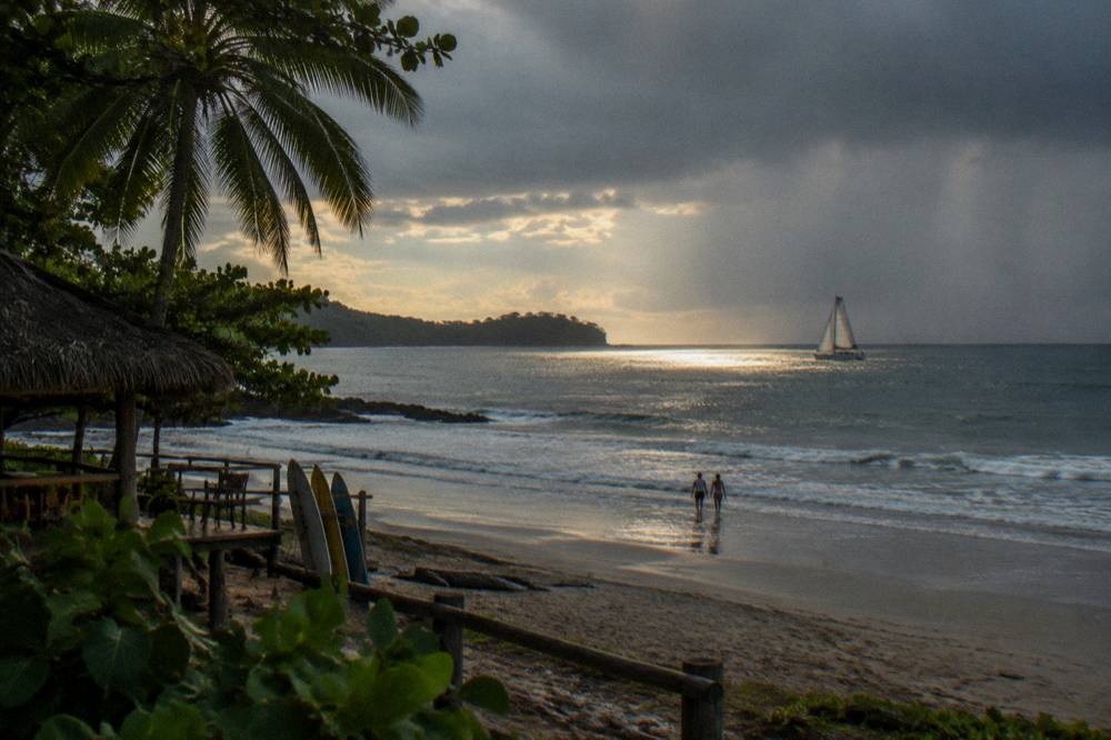Rain shower passing over darkening ocean while a boat sails in sunlight nearby