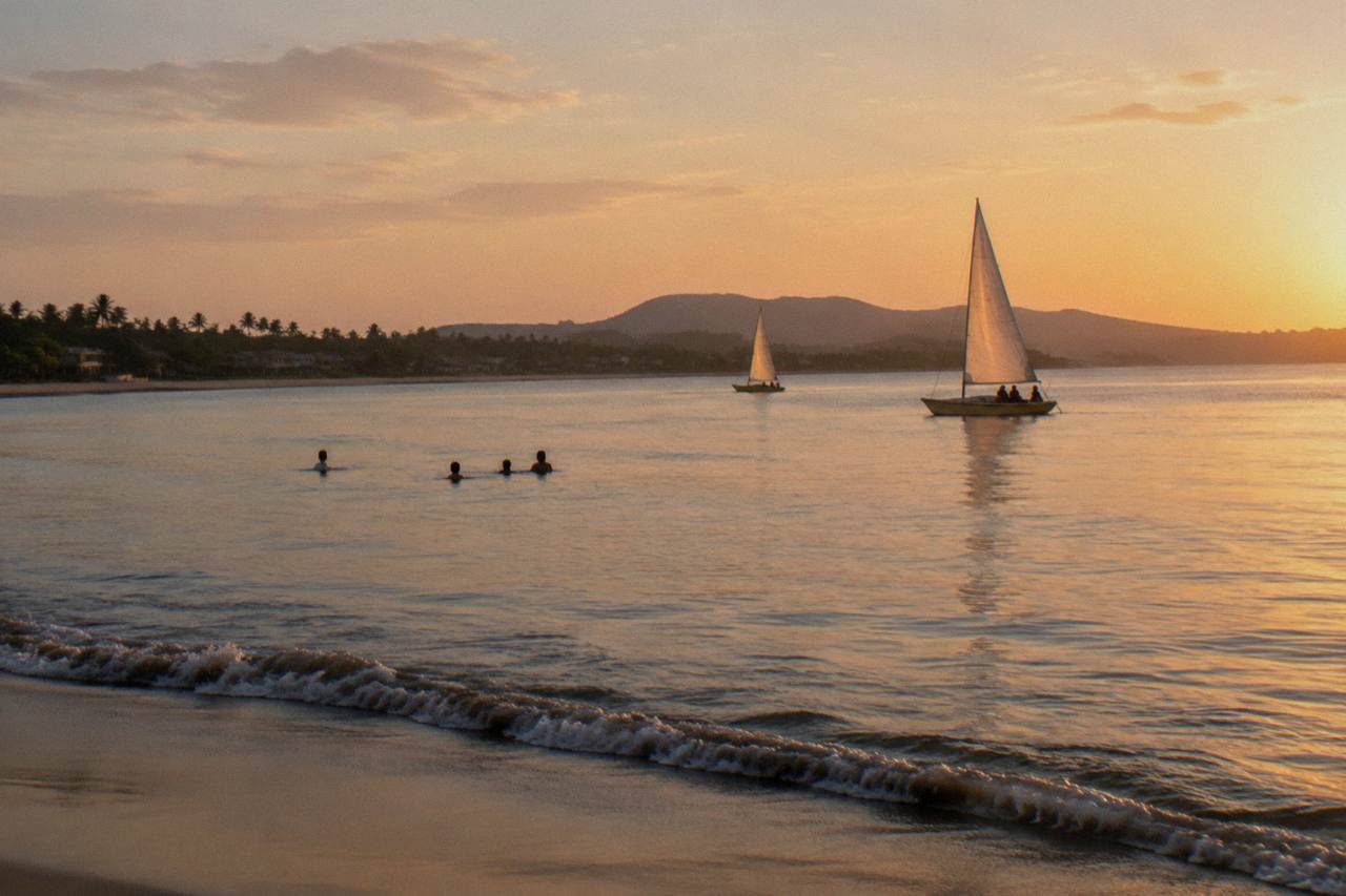 Catamaran sails on calm golden water off a tropical beach coastline at late afternoon