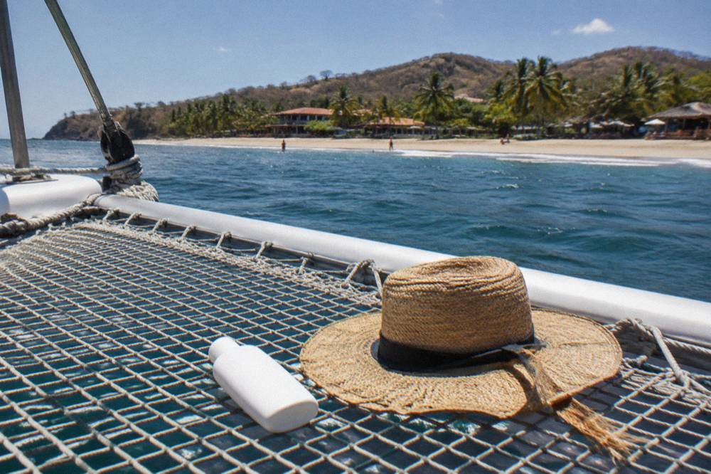 Sunscreen bottle and wide-brim hat resting on a catamaran deck in bright tropical light