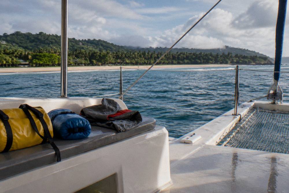 Dry bags and rain jackets stowed on a catamaran bench under clearing tropical sky