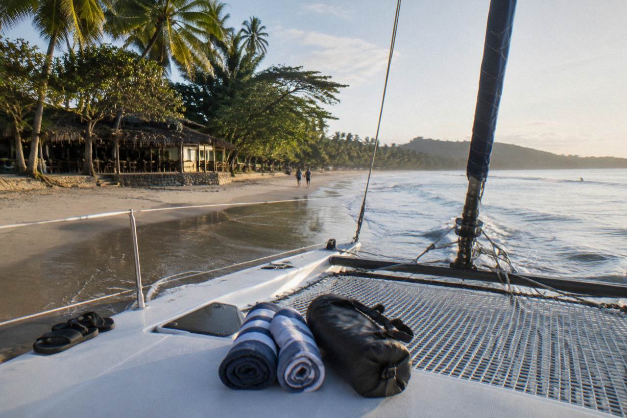 Catamaran deck with dry bags and towels laid out before departure from a tropical beach